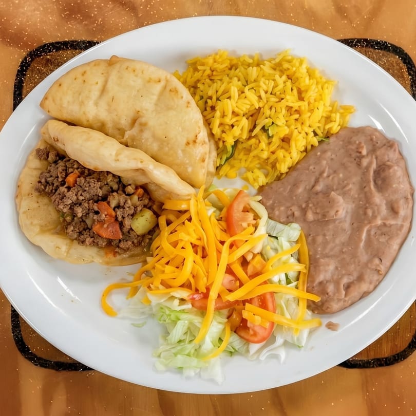 A plate of Mexican food with two gorditas, yellow rice, refried beans, and a side salad.